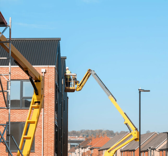 Builders working off Telescopic Boom Lift while fitting insulated sandwich panels to the facade of a new multistorey residential building. Working at height safely